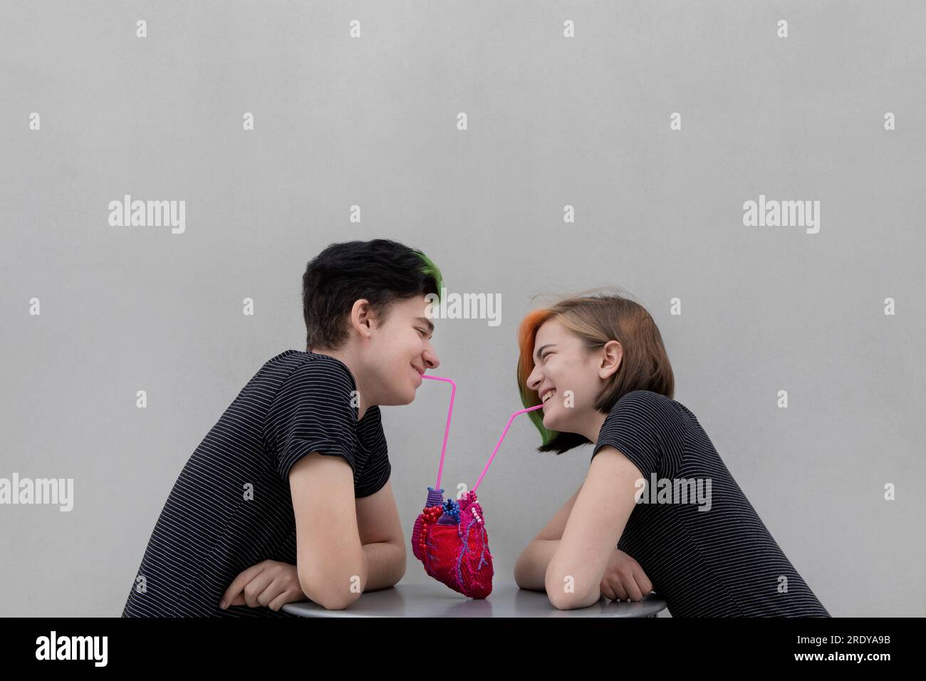 Joyeux couple d'adolescents buvant de coeur sur fond gris Banque D'Images