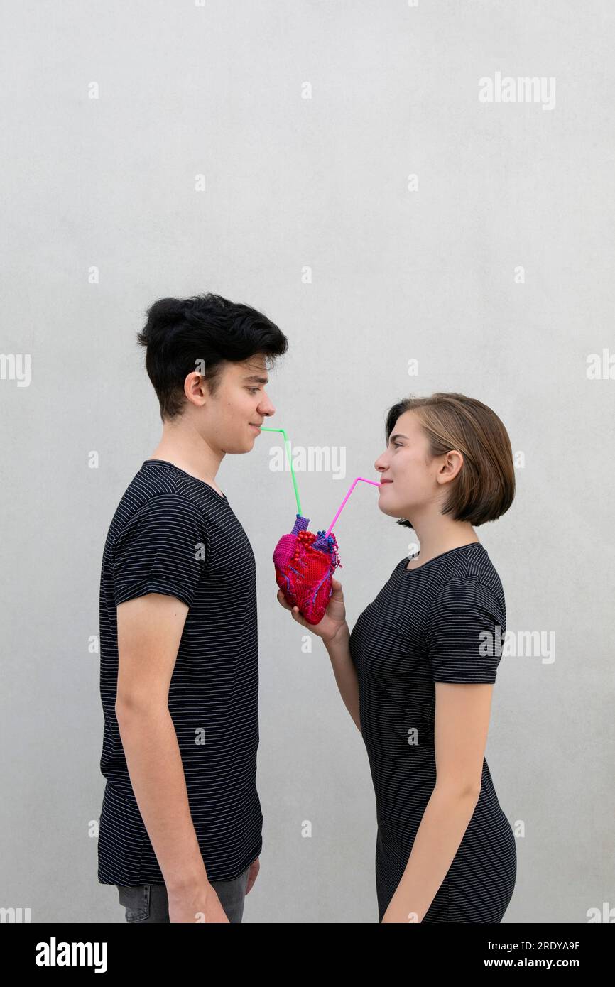 Couple d'adolescents buvant avec de la paille du coeur modèle sur fond gris Banque D'Images
