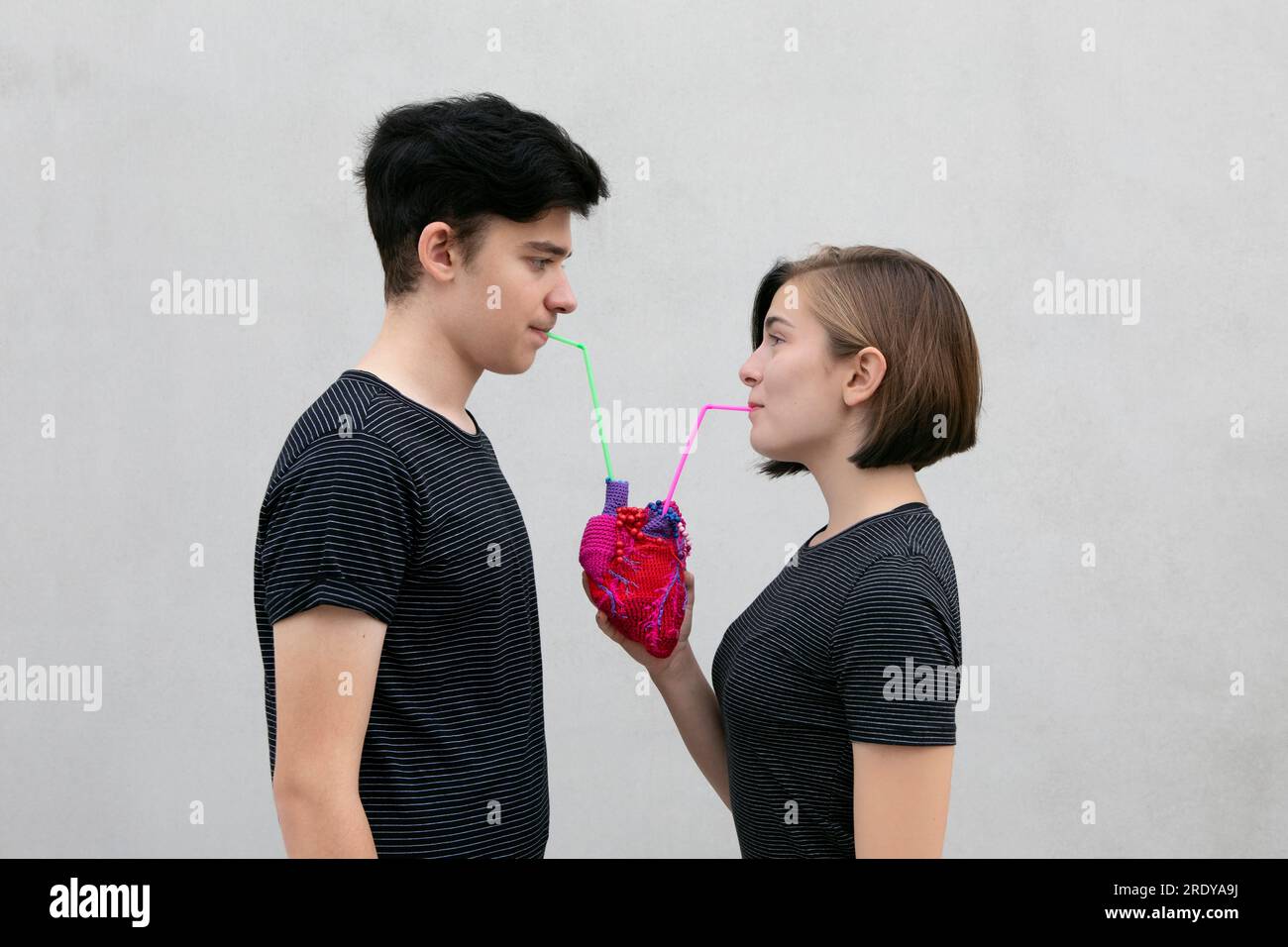 Couple d'adolescents buvant ensemble de coeur modèle sur fond gris Banque D'Images