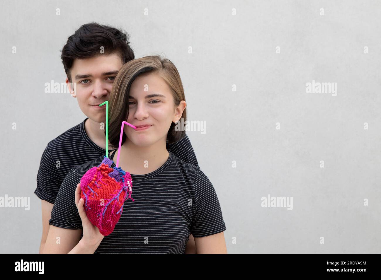 Couple d'adolescents souriants buvant ensemble du coeur modèle sur fond gris Banque D'Images