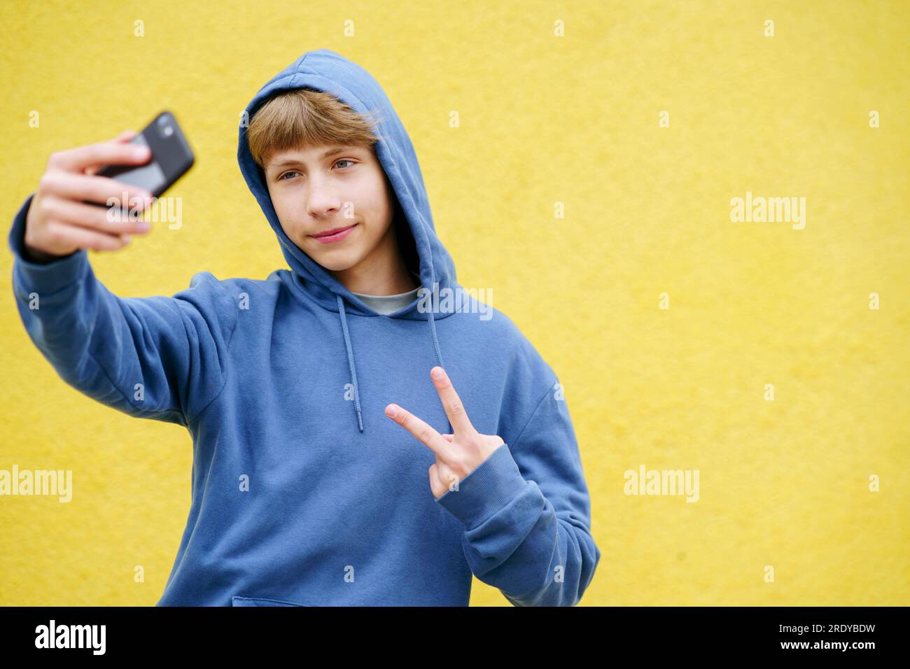 Garçon souriant montrant geste de signe de paix et prenant selfie par téléphone intelligent Banque D'Images