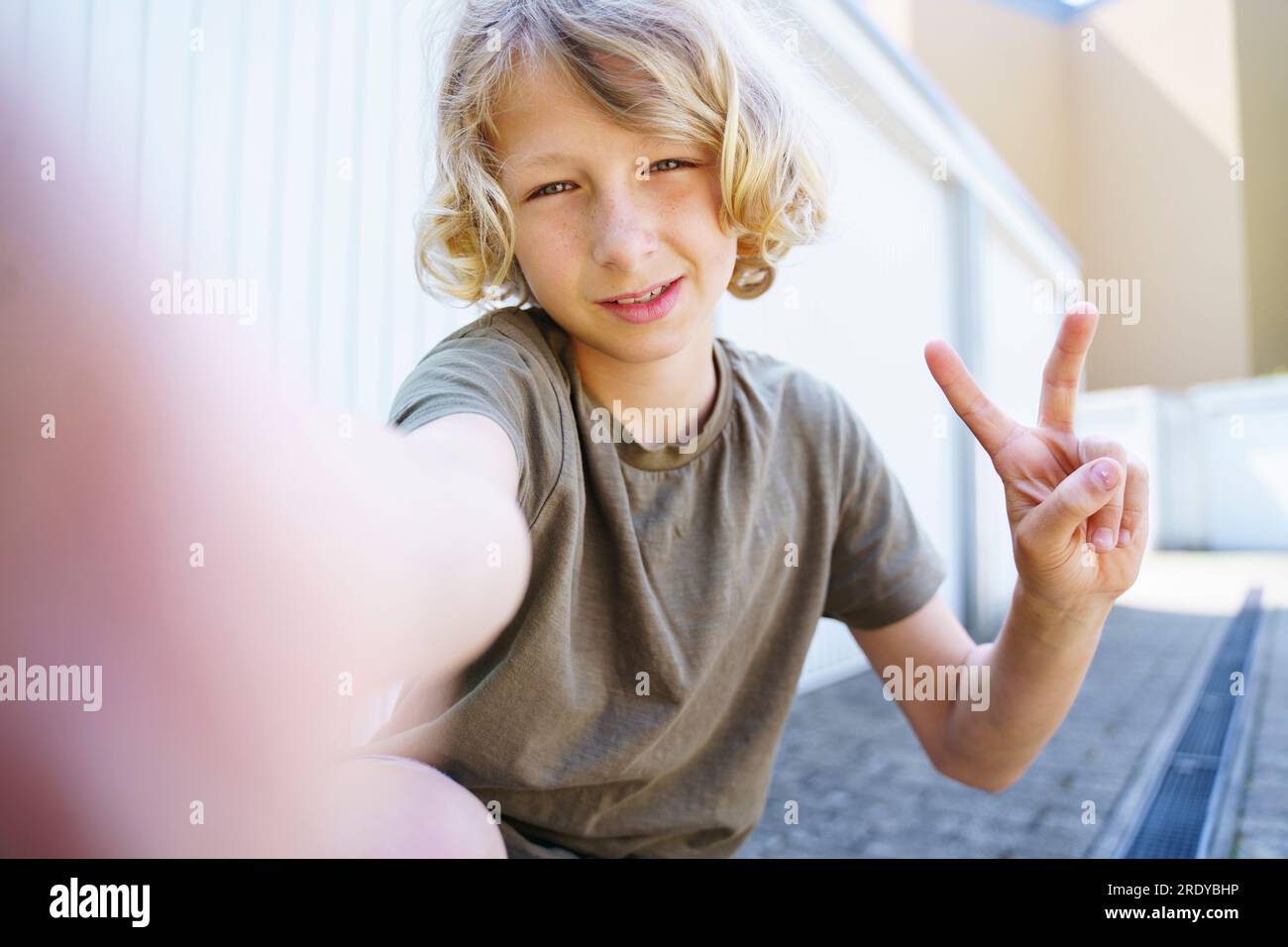 Garçon aux cheveux blonds montrant signe de paix à l'extérieur du garage Banque D'Images