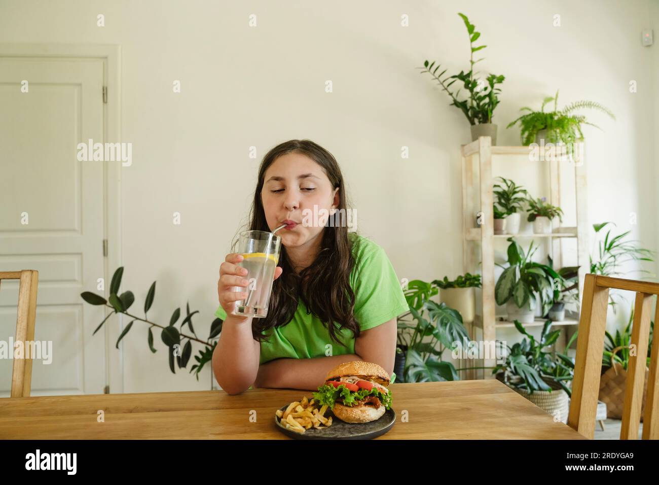 Fille buvant du soda du verre avec hamburger sur la table à la maison Banque D'Images