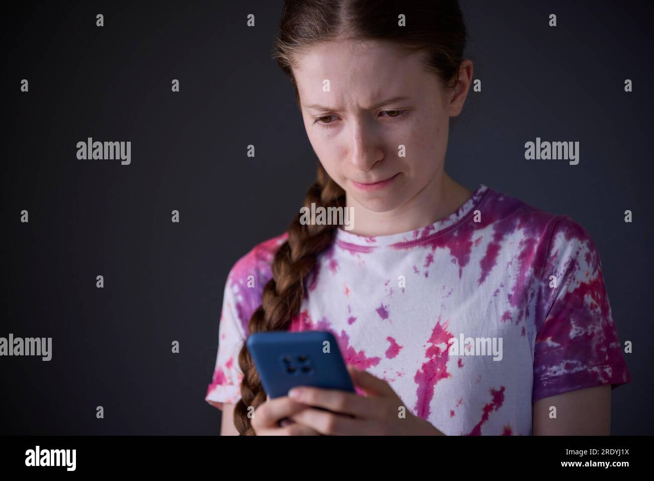 Studio Shot de Stressed Teenage Girl avec téléphone portable intimidé en ligne Banque D'Images