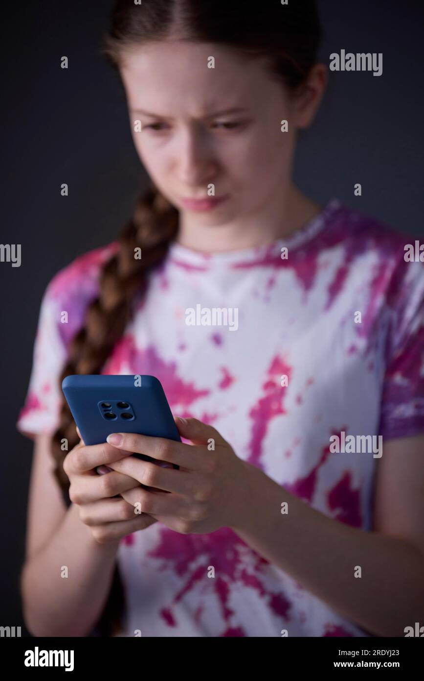 Studio Shot de Stressed Teenage Girl avec téléphone portable intimidé en ligne Banque D'Images