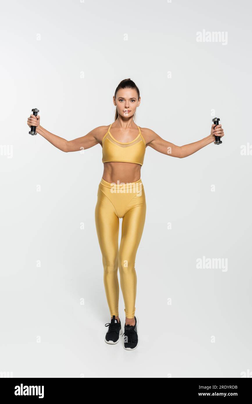 femme dans la formation de vêtements de fitness avec des haltères et regardant la caméra sur fond blanc Banque D'Images