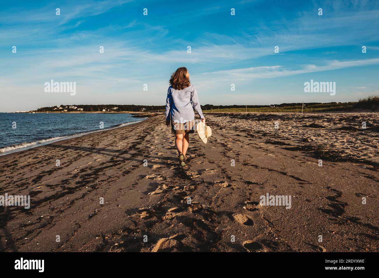 Femme mature se promenant sur la plage de Cape Cod avec le chapeau à la main Banque D'Images