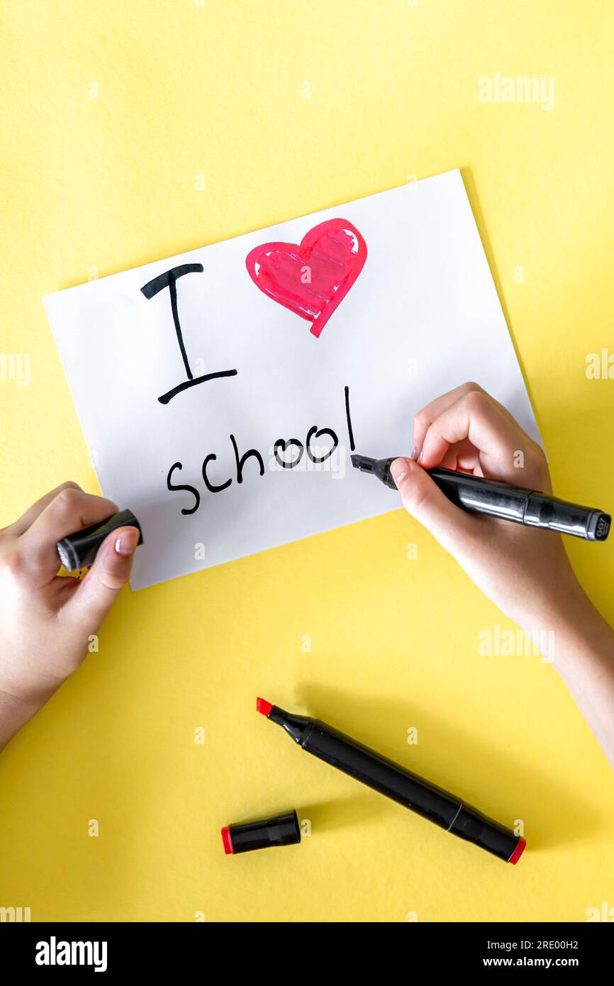 J'aime l'école la main de l'enfant écrit dans un papier sur un fond jaune. Banque D'Images