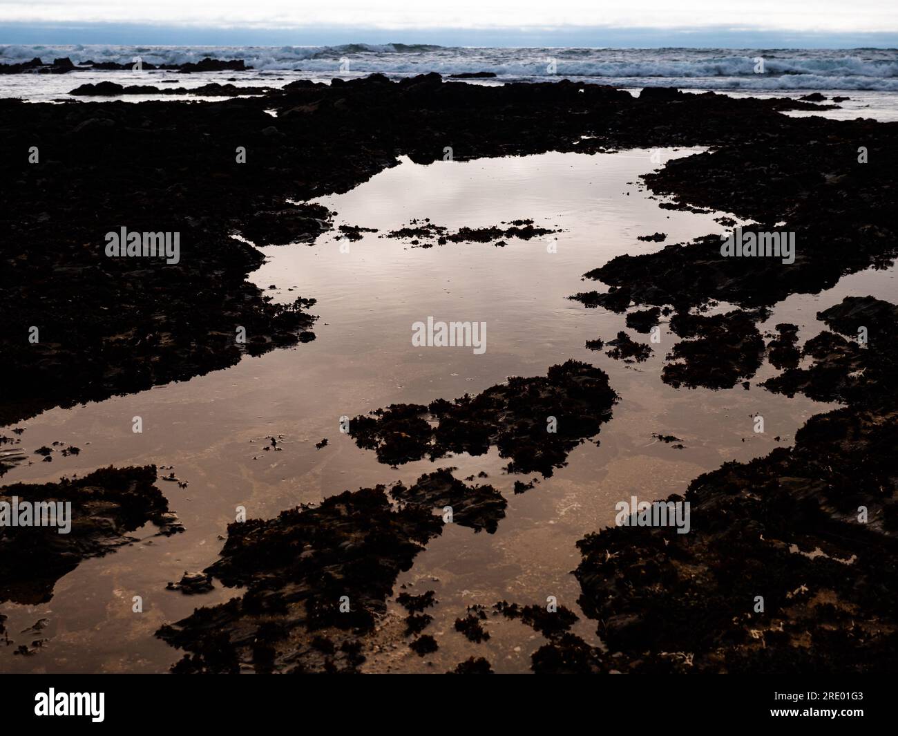 Piscine à marée rocheuse au bord de l'océan réfléchissant le ciel Banque D'Images