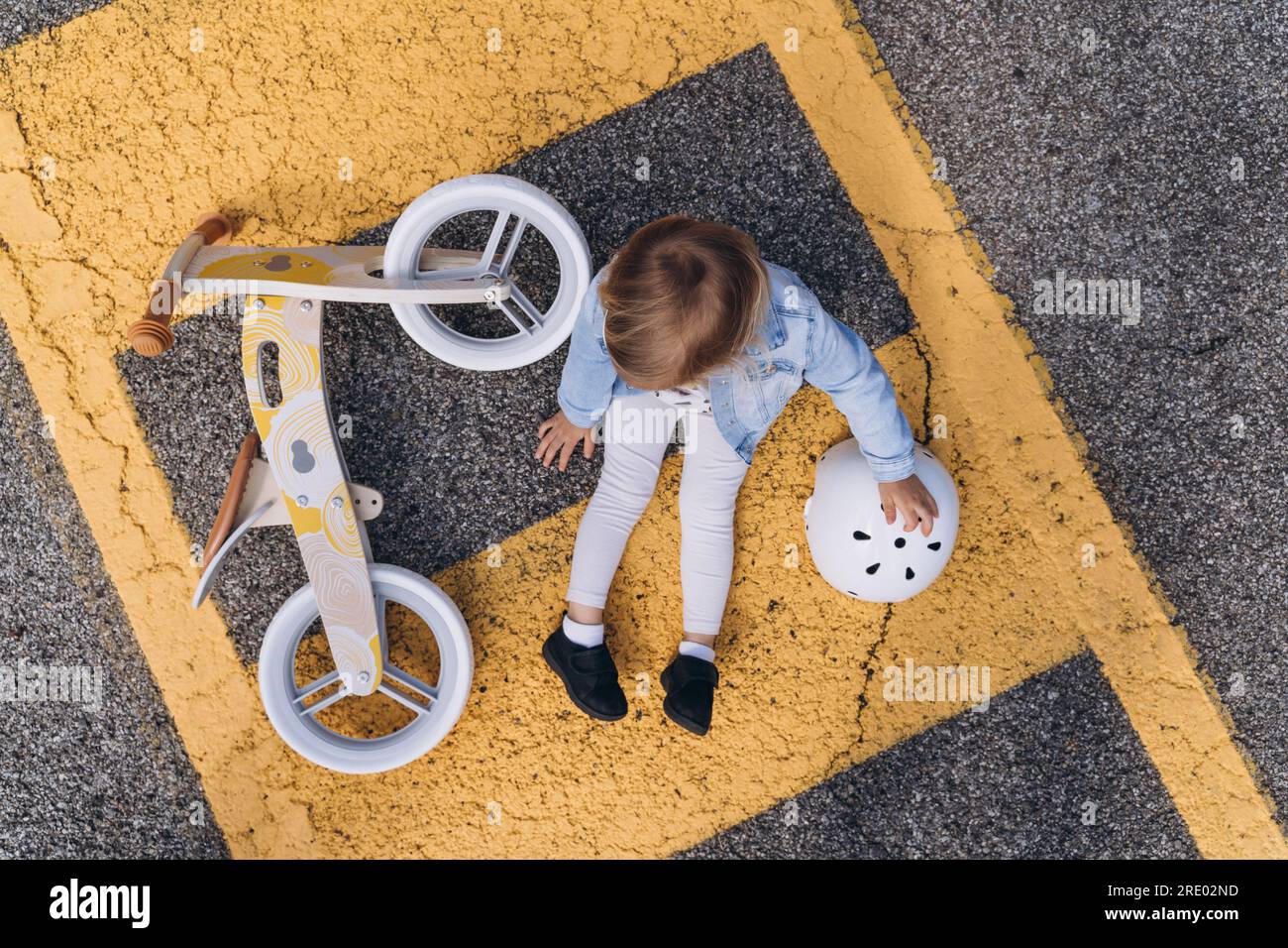 Une fillette est assise sur le trottoir à côté d'un vélo d'équilibre Banque D'Images