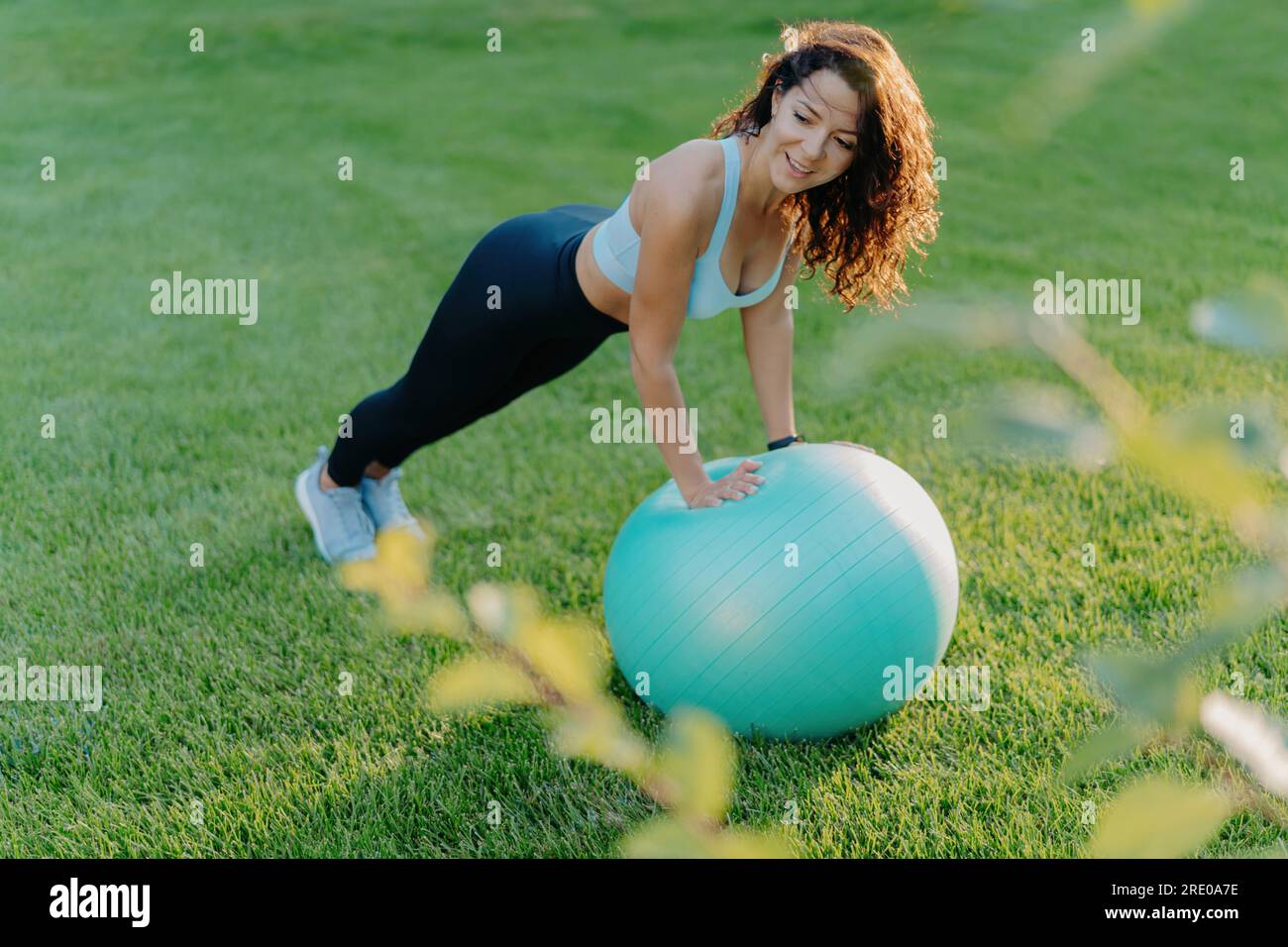 Slim Woman aime les exercices de gymnastique sur pelouse verte avec FIT ball, portant des vêtements actifs. Adopte un mode de vie sain et actif. Concept de fitness. Banque D'Images