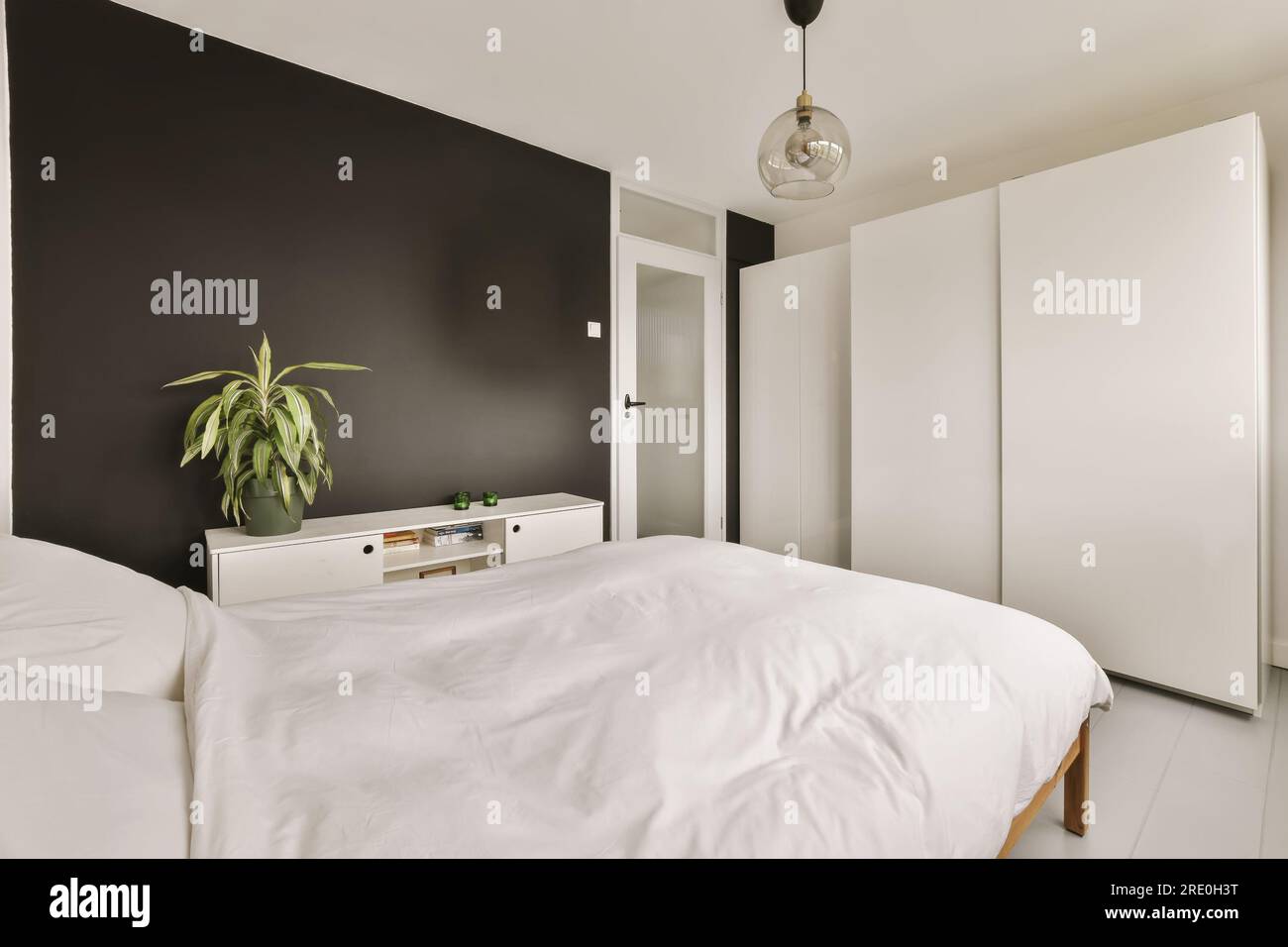 une chambre avec des murs noirs et des draps blancs sur le lit, il y a une plante dans le coin de la pièce Banque D'Images