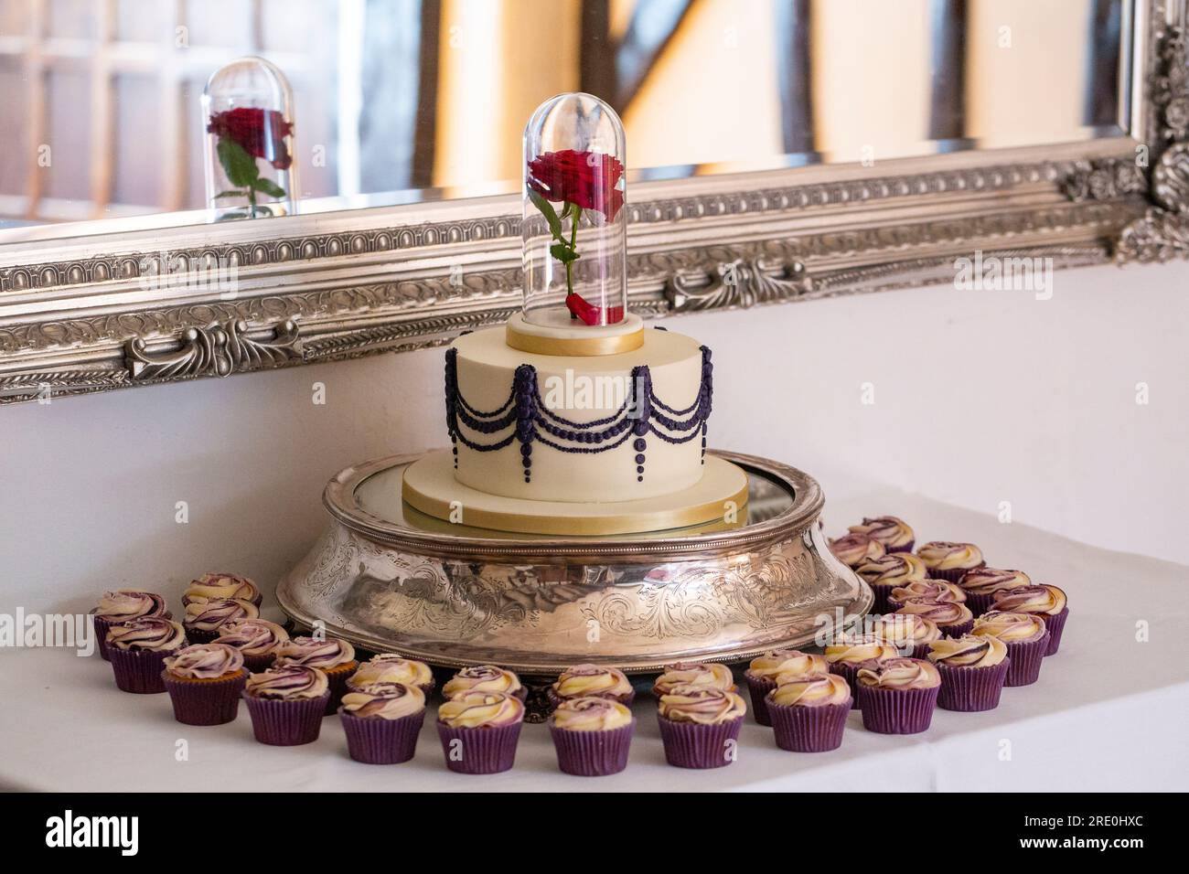 Gâteau de mariage avec une rose rouge dans un bocal en verre, entouré de cupcakes à motifs roses Banque D'Images