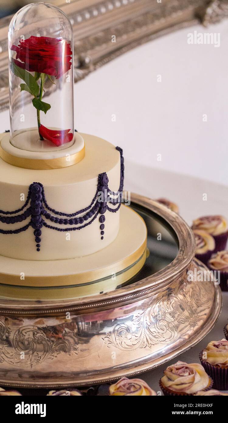 Gâteau de mariage avec une rose rouge dans un bocal en verre, entouré de cupcakes à motifs roses Banque D'Images