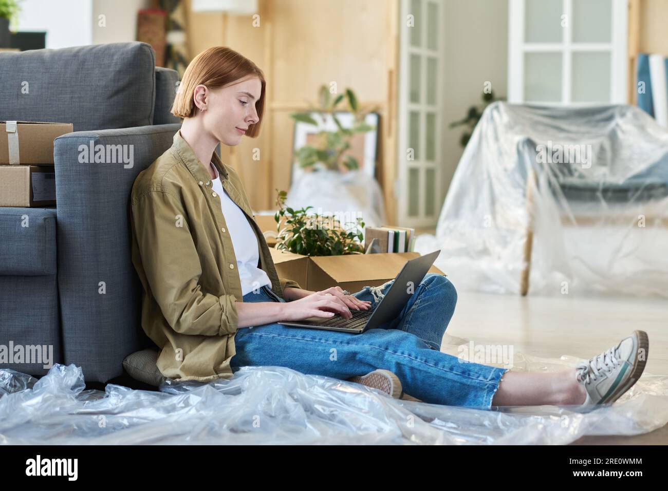 Vue de côté de jeune femme solopreneur dans casualwear assis sur le sol par  canapé dans le salon et tapant sur le clavier d'ordinateur portable tout en  réseau Photo Stock - Alamy