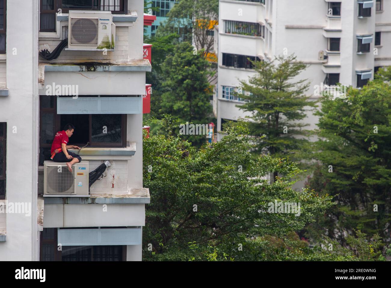 Un technicien chinois est assis sur l'unité de climatisation dans un foyer surélevé pour des travaux de réparation, un travail de service à haut risque qui nécessite un travail en hauteur. Banque D'Images