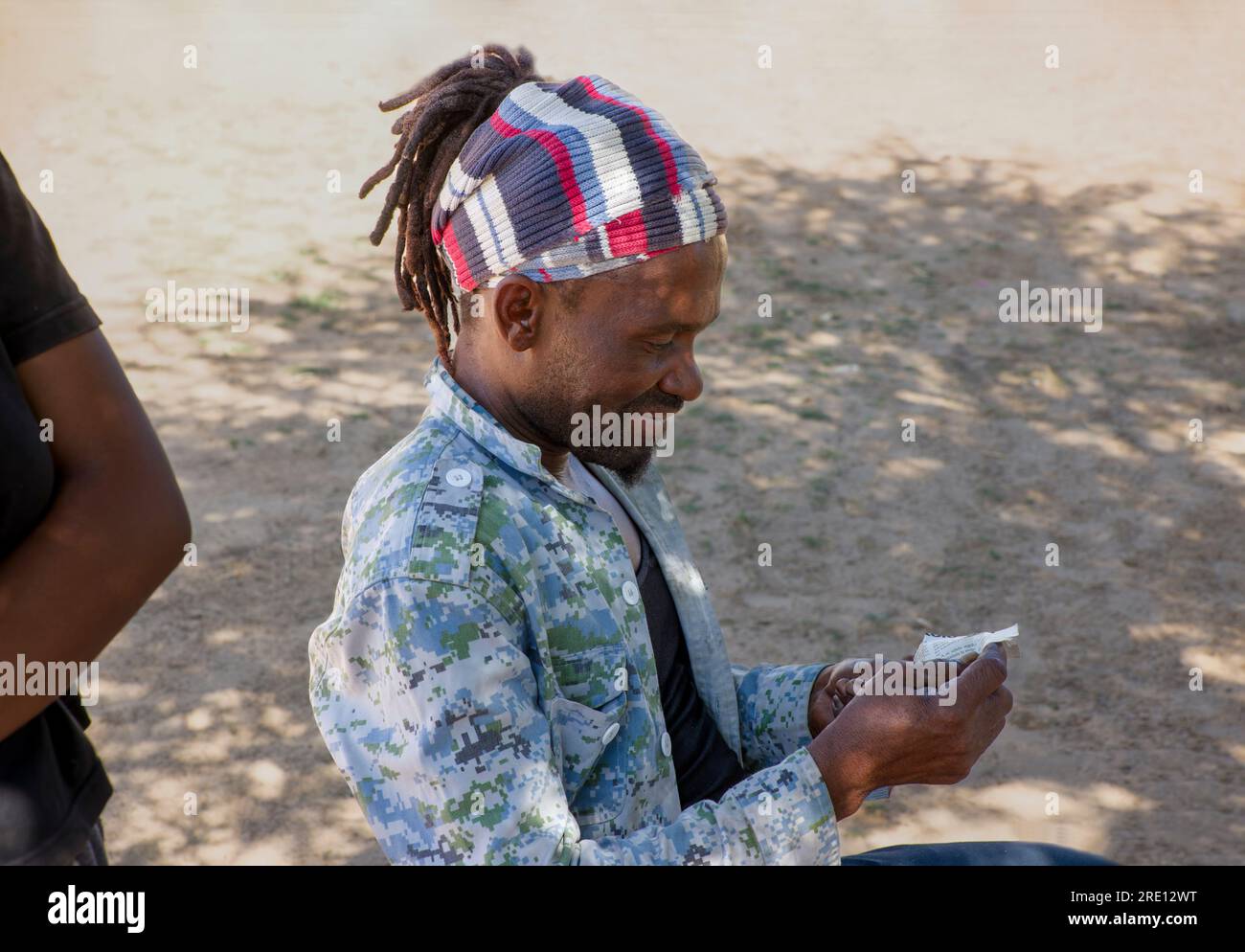 homme rasta avec des dreadlocks dans le village, lisant une coupure de journal, posant dans la cour Banque D'Images