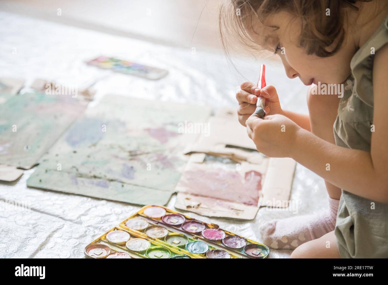 Douce petite fille jouant avec des peintures. Enfant explorant sa créativité en peignant avec des aquarelles dans un environnement domestique. Banque D'Images