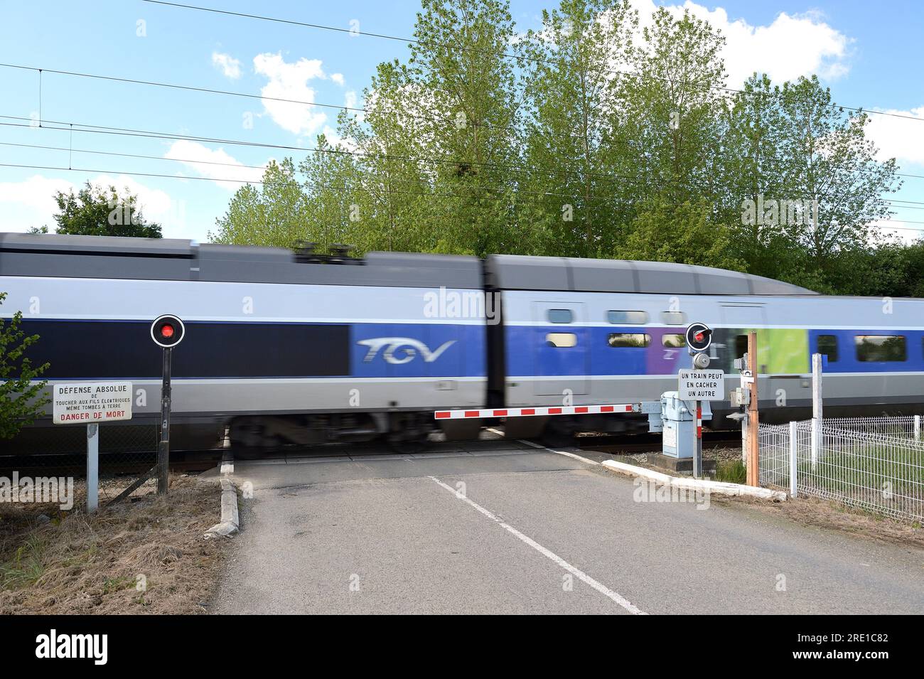 Passage à niveau sur une route de campagne avec portail ferroviaire automatique. Portails automatiques abaissés, portails fermés, feu rouge clignotant et TGV à grande vitesse passi Banque D'Images