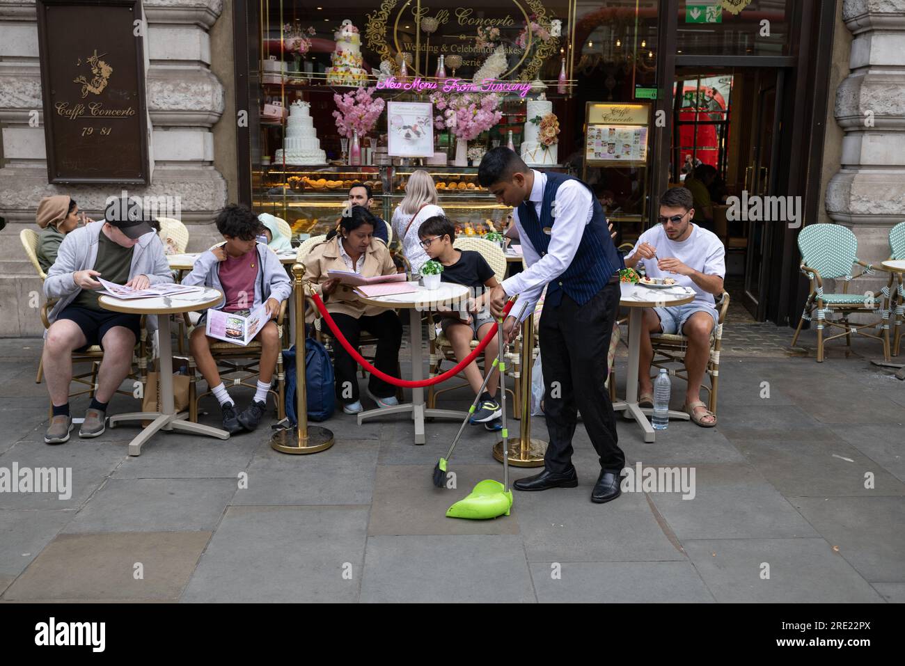 Un serveur nettoie le trottoir devant un café Concerto dans le West End de Londres, alors que les touristes affluent vers la capitale cet été, le 16 juillet 2023, en Angleterre. Banque D'Images