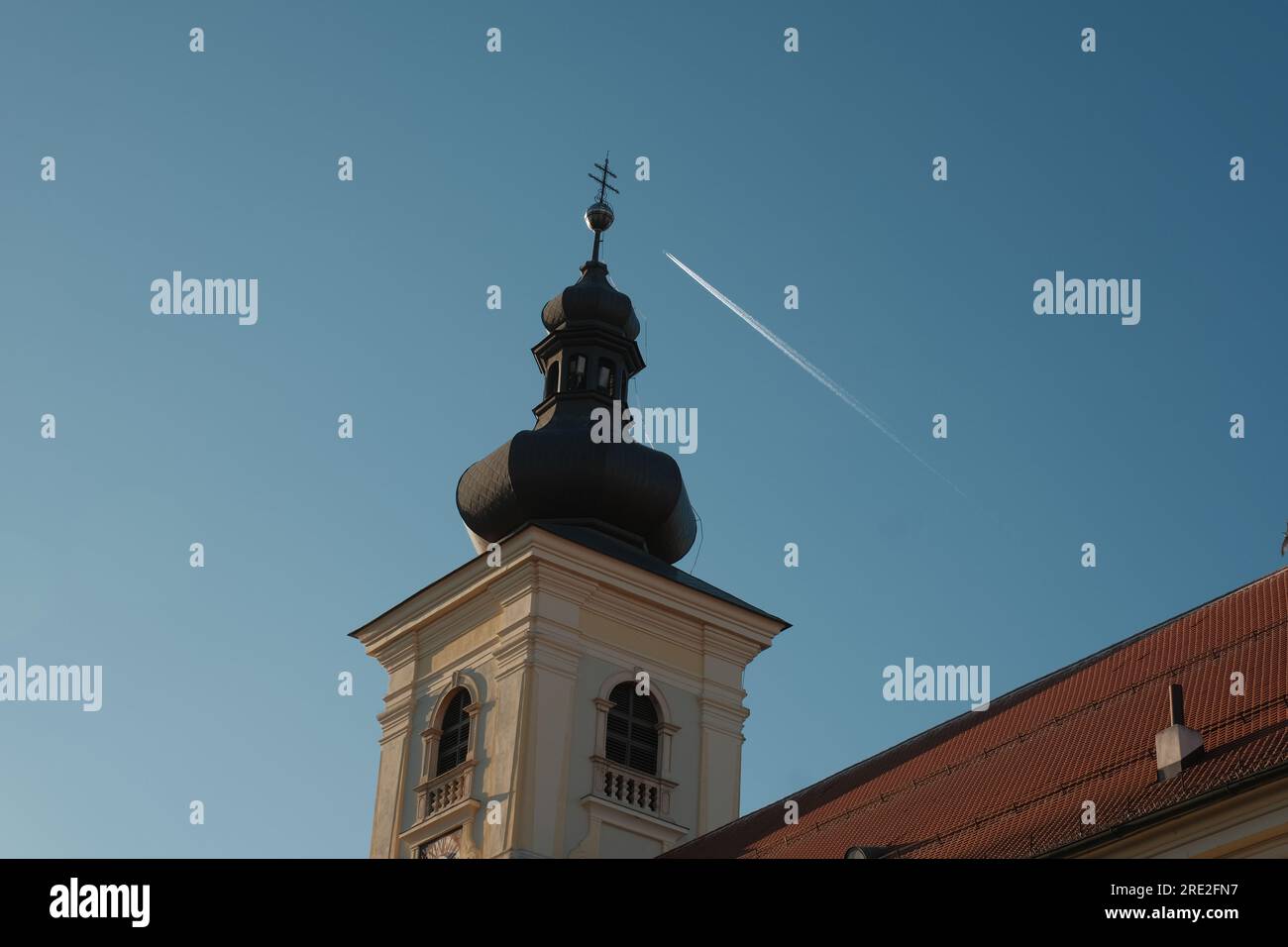 Un gros plan détaillé d'une tour d'église roumaine, avec l'élément surprise d'un avion en arrière-plan, posé contre le ciel bleu expansif. Banque D'Images