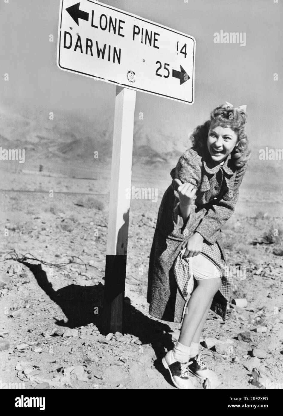 Californie : 1955 l'actrice Lori Nelson montre de manière ludique quelques jambes et des autostop tout en filmant sur place près du mont. Whitney. Banque D'Images