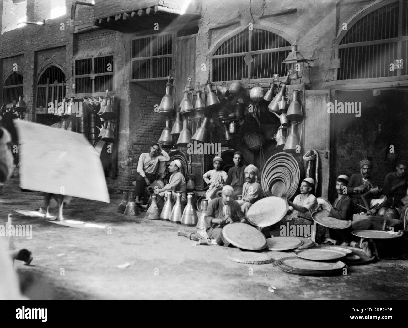 Bagdad, Irak 1932 Une scène de rue à Bagdad avec la lumière du soleil qui coule sur des magasins de cuivre vendant des cruches et des plateaux. Banque D'Images