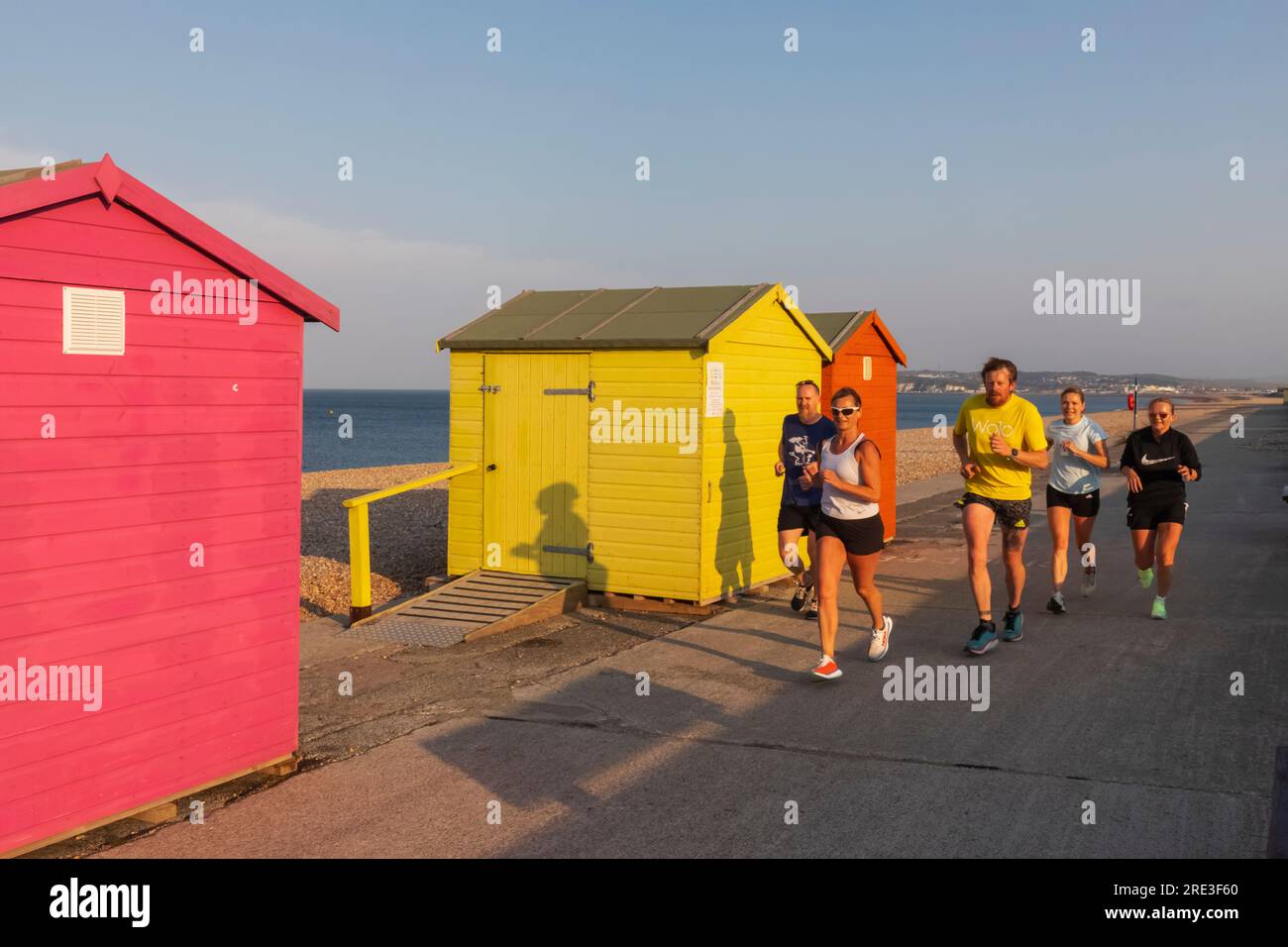 Angleterre, Sussex, East Sussex, Seaford, cabanes colorées en bord de mer et joggeurs tôt le matin Banque D'Images