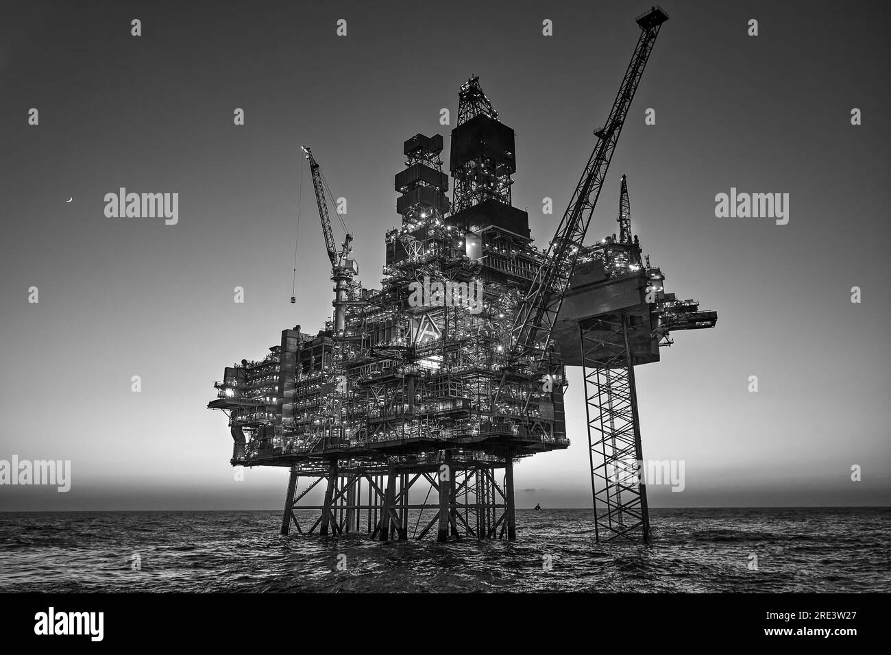 Photo noir et blanc d'une plate-forme pétrolière Jack up dans la mer au coucher du soleil. Banque D'Images