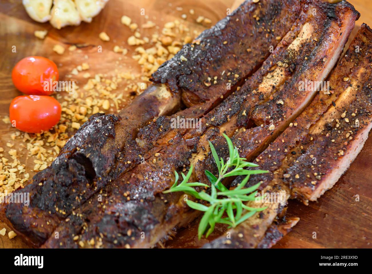 Côtes de porc cuites sur une assiette en bois Garnir avec de l'ail, des tomates et des légumes verts. Banque D'Images