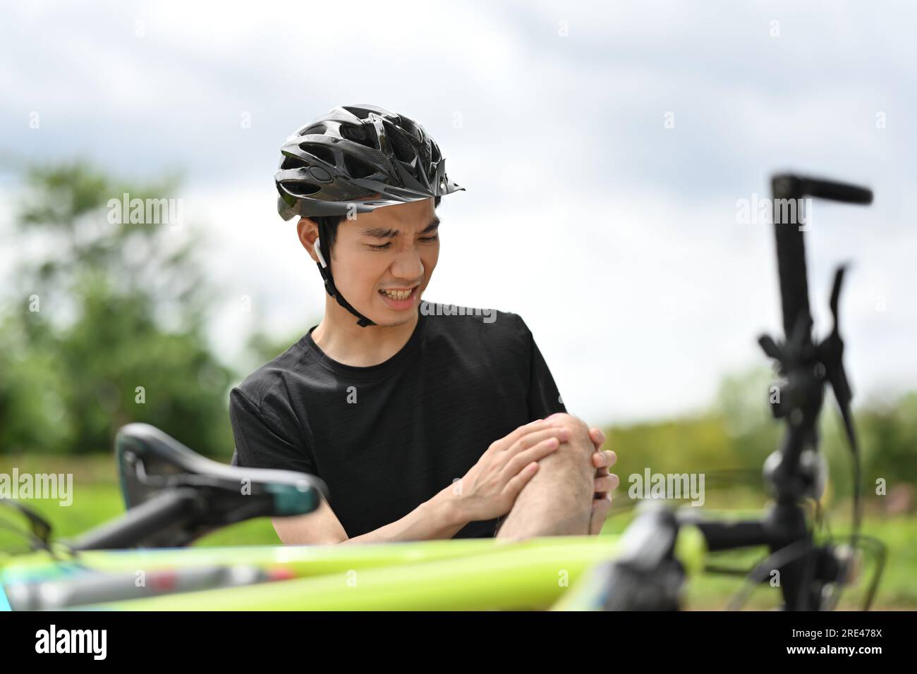 Cycliste masculin assis sur le sol, se blessant au genou après un accident de vélo Banque D'Images