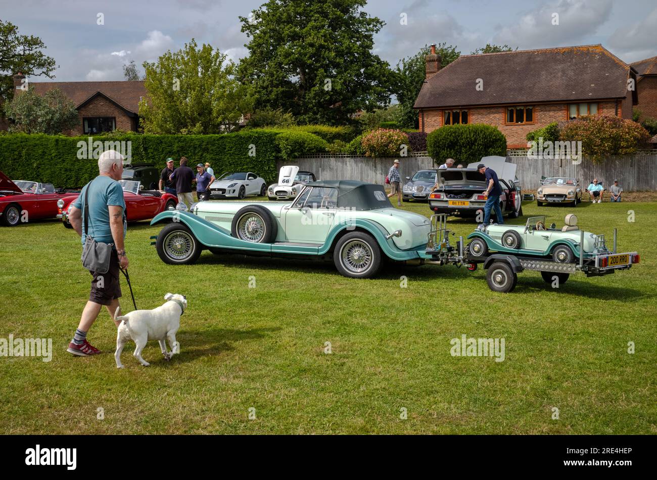Un homme avec un chien marche près d'une voiture classique Durow Cars 'Vintage de ville' kit remorquant un traîneau transportant sa réplique lors d'un salon de voitures classiques à Storrington Banque D'Images