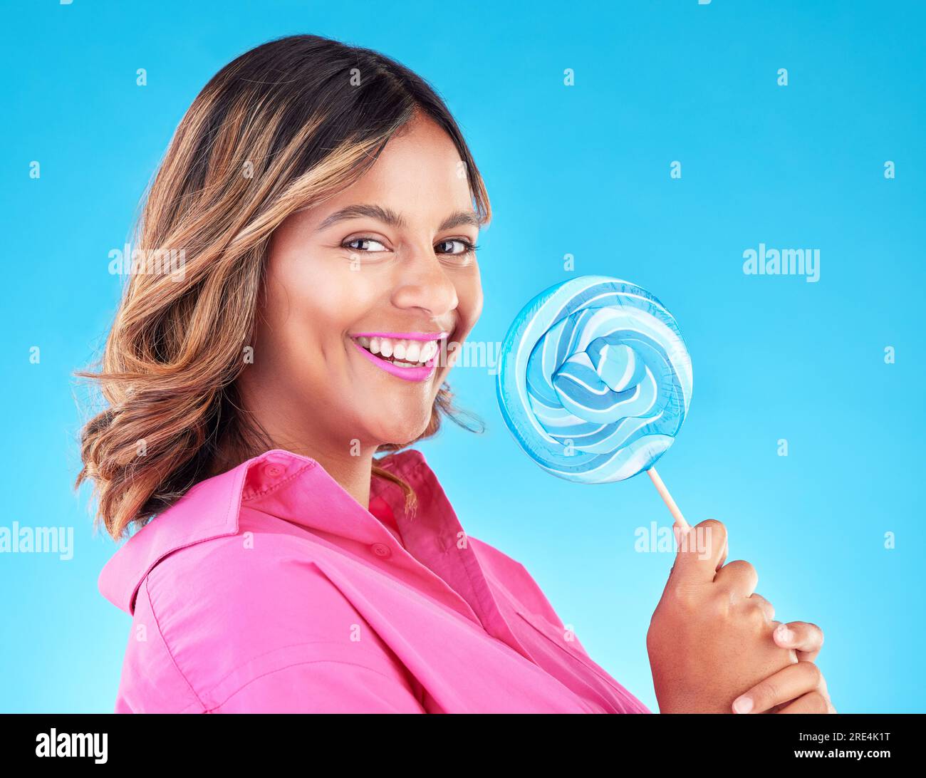 Femme, sucette et sourire dans le portrait de studio avec manger, bonbons et excité pour la nourriture par fond bleu. Fille, étudiante ou jeune mannequin avec Banque D'Images