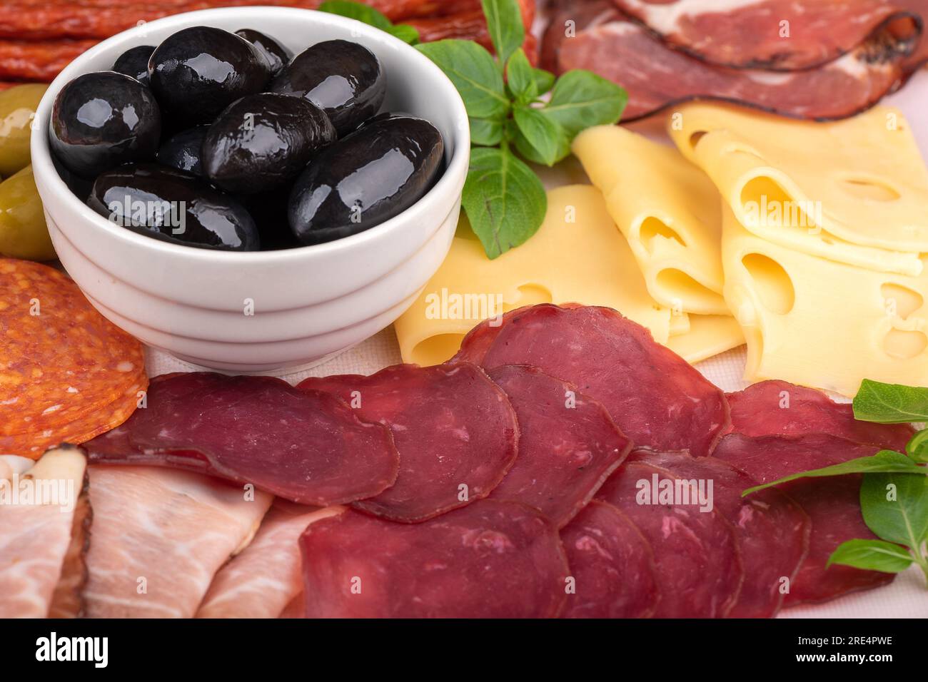 Gros plan d'olives dans un bol blanc, prosciutto tranché et fromage, basilic vert. Coupes de viande, fromage et différents types de saucisses. Banque D'Images