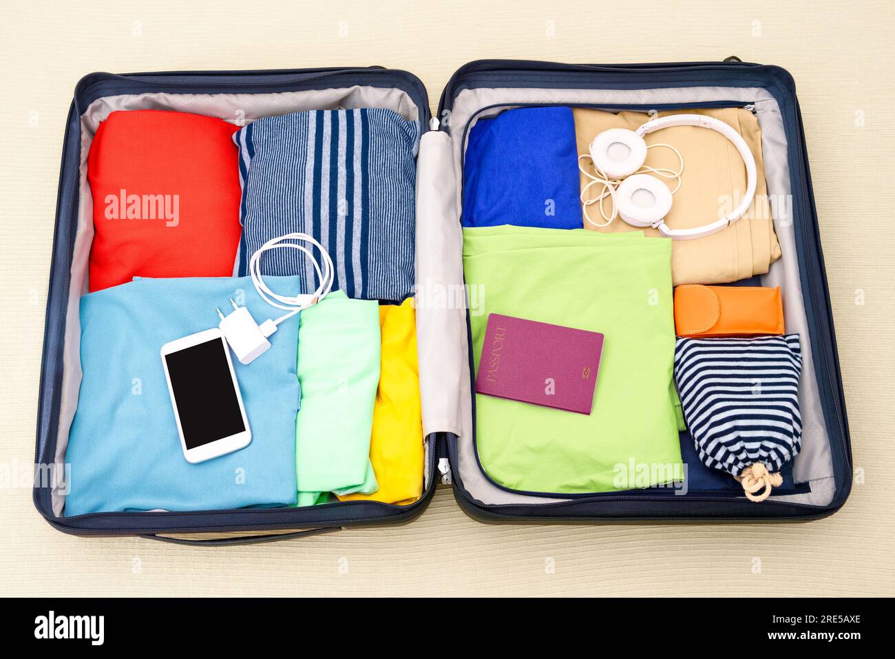 Voir le formulaire ci-dessus d'une valise ouverte emballée avec des vêtements, des accessoires et un passeport sur un lit. Concept de voyage. Banque D'Images