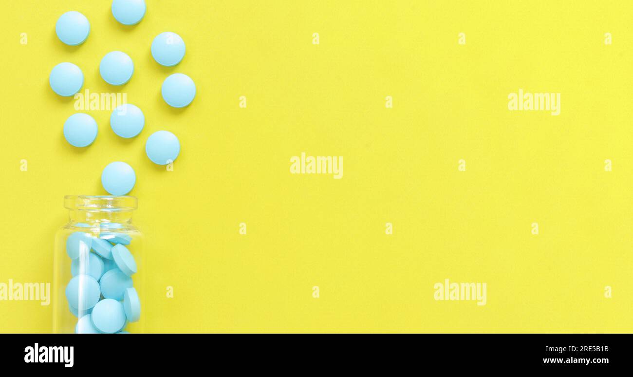 Les pilules bleues sont versées dans une bouteille en verre sur un fond jaune. Complexe de vitamine B, vue de dessus, espace de copie. Soins de santé, pilules médicales et diététique su Banque D'Images