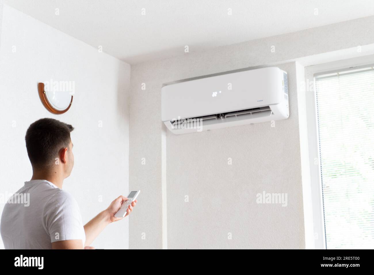 Un jeune homme active la climatisation. Beau jeune homme allumant le climatiseur avec télécommande. Hausse des températures, temps chaud. Banque D'Images