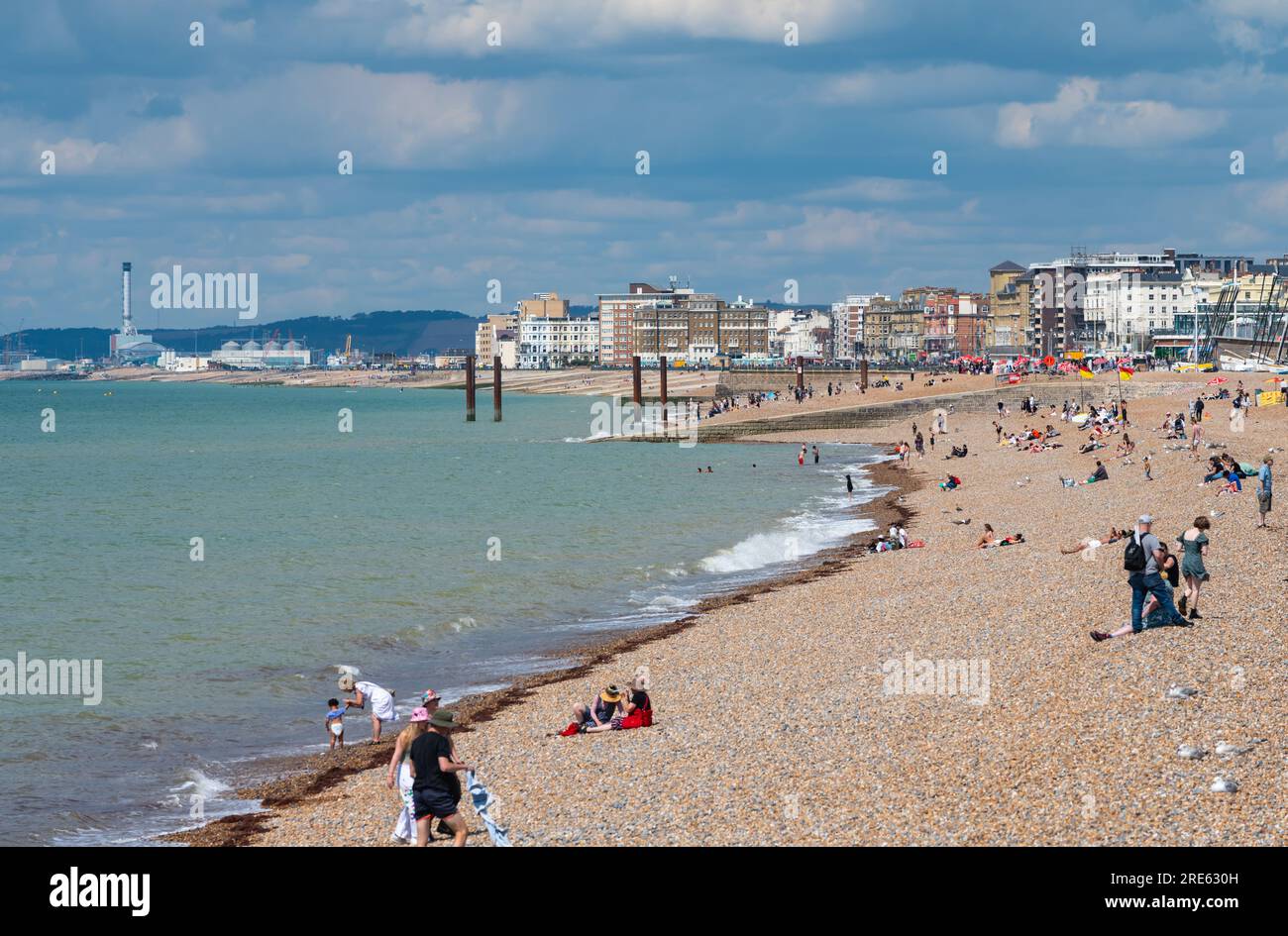 Les gens sur la plage regardant vers l'ouest le long de la côte, sur une nuageuse nuageuse journée d'été à la station balnéaire britannique de Brighton & Hove, Royaume-Uni. Banque D'Images