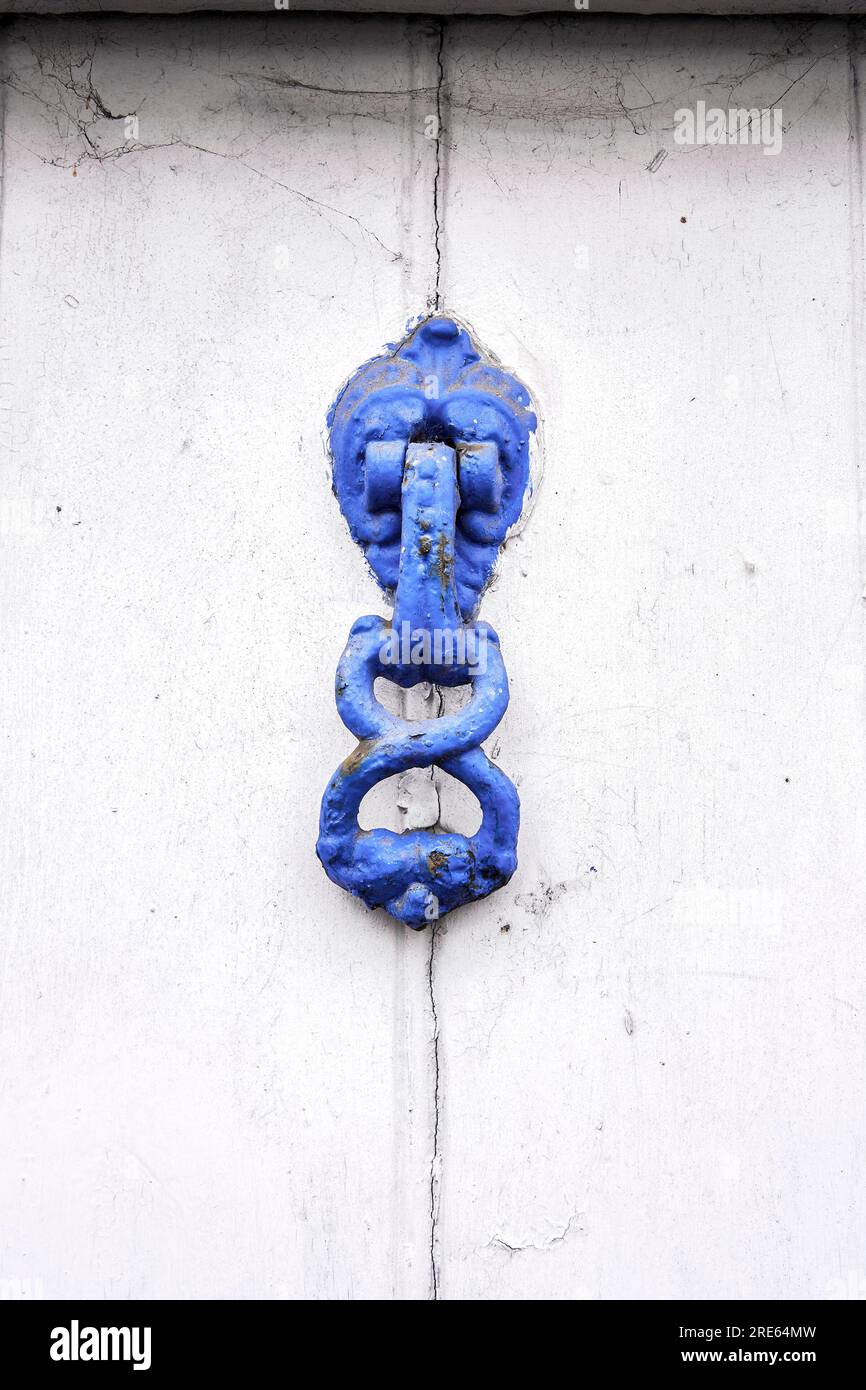 Vieux heurtoir de porte peint en bleu sur la porte blanche Banque D'Images