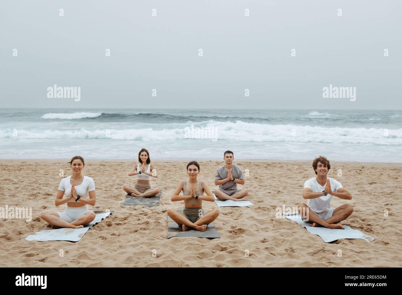 Yoga de plage pour les jeunes. Hommes et femmes méditant ensemble sur la rive de l'océan, assis sur des nattes en position lotus Banque D'Images