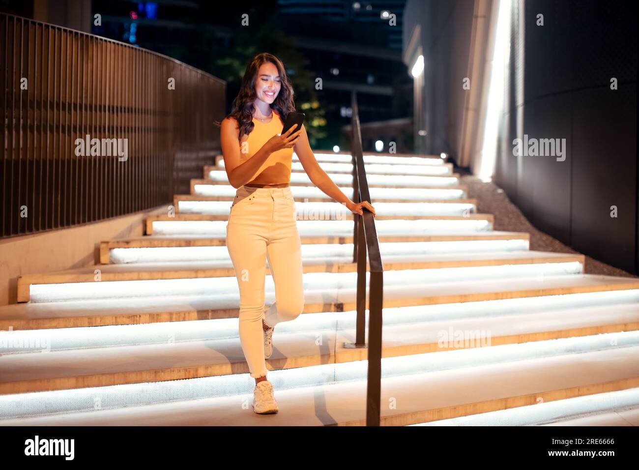 Plan en longueur de femme à l'aide du téléphone pendant la marche de nuit dans la ville, en descendant les escaliers illuminés, espace libre Banque D'Images