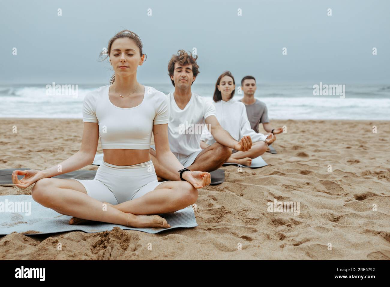 Vue sur l'océan Les gens calmes assis dans la pose de lotus tenant les doigts dans le geste de la main de gyan mudra, méditant sur la plage Banque D'Images