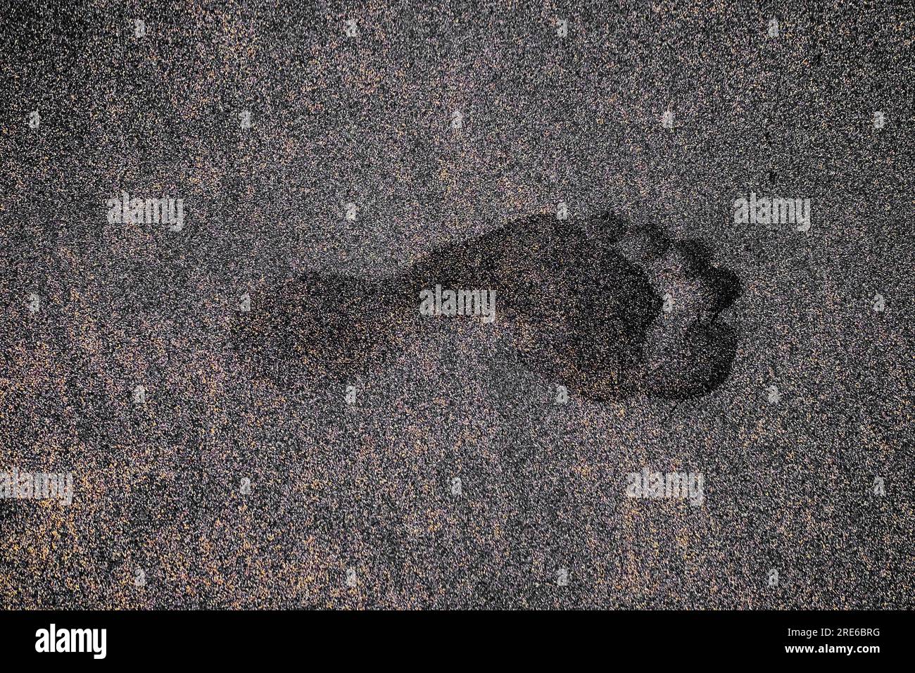 Empreinte unique profonde du pied humain gauche dans le sable volcanique sombre. Banque D'Images