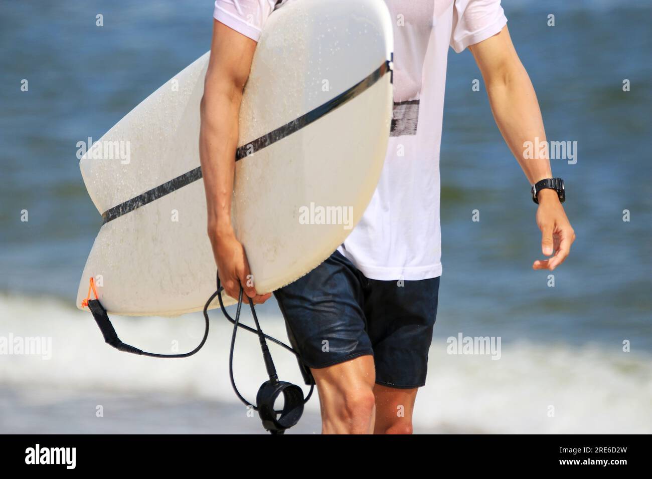 Gros plan d'un mâle portant sa planche de surf marchant à Gilgo Beach près de l'océan sur long Island. Banque D'Images