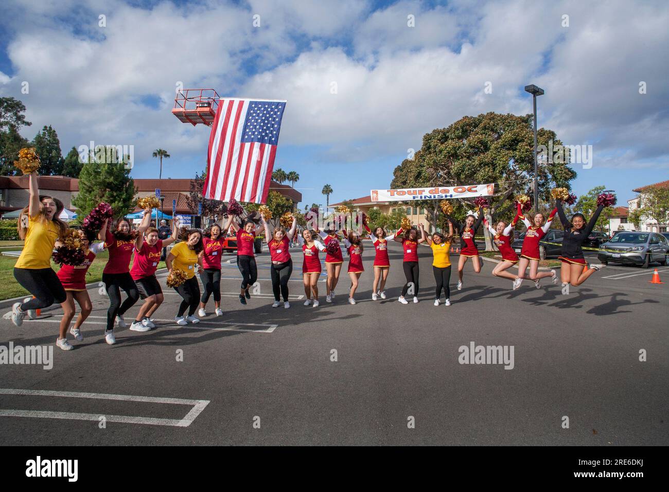 Costa Mesa. 21 mai 2016. Un drapeau américain flotte dans le vent alors que les cheerleaders locaux du lycée saluent les cyclistes quittant la ligne de départ d'une course caritative de 55 miles à Costa Mesa, Californie. (Image de crédit : © Spencer Grant/ZUMA Press Wire) USAGE ÉDITORIAL SEULEMENT! Non destiné à UN USAGE commercial ! Banque D'Images