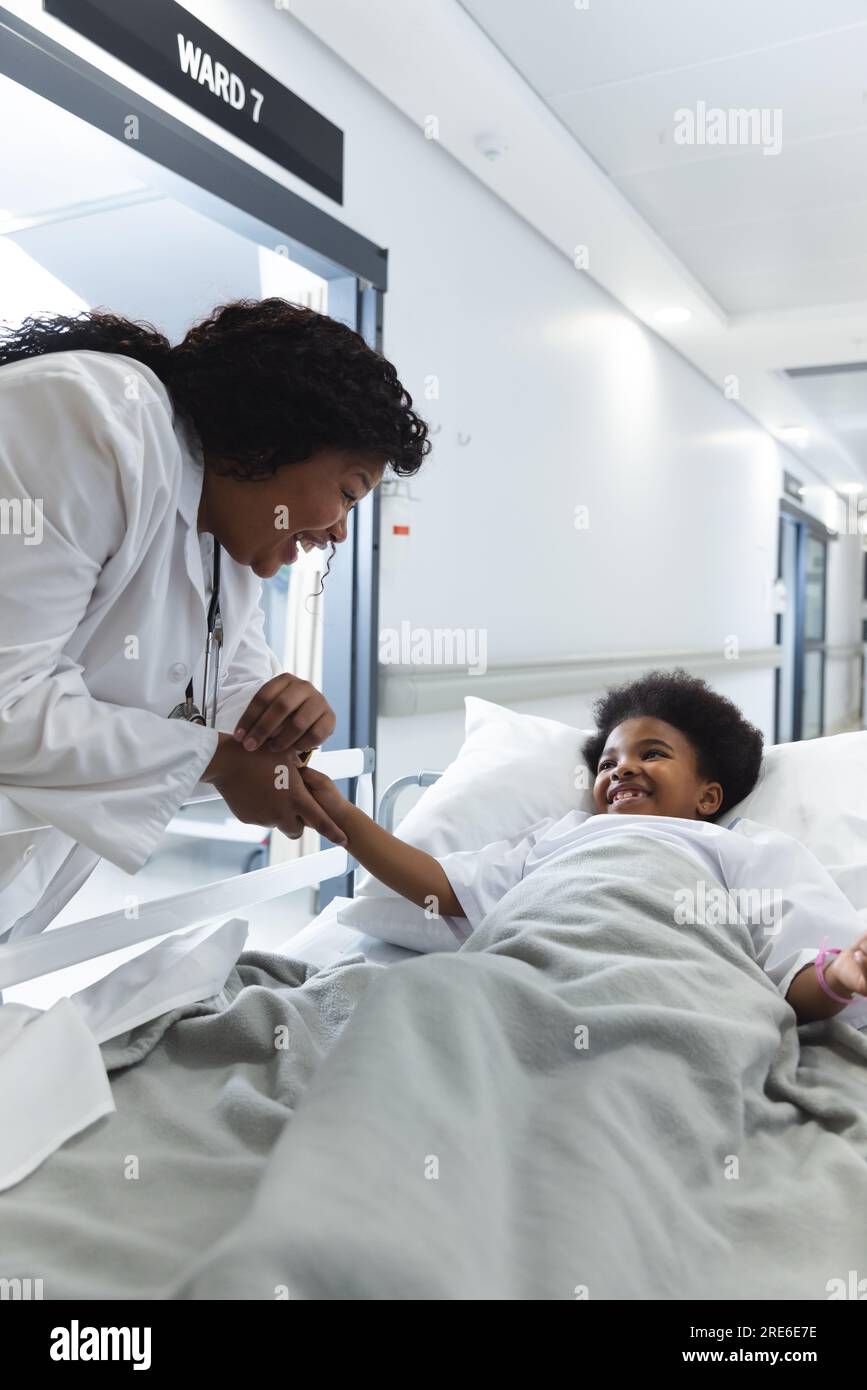 Médecin afro-américaine parlant à une patiente fillette allongée sur le lit dans le couloir à l'hôpital Banque D'Images