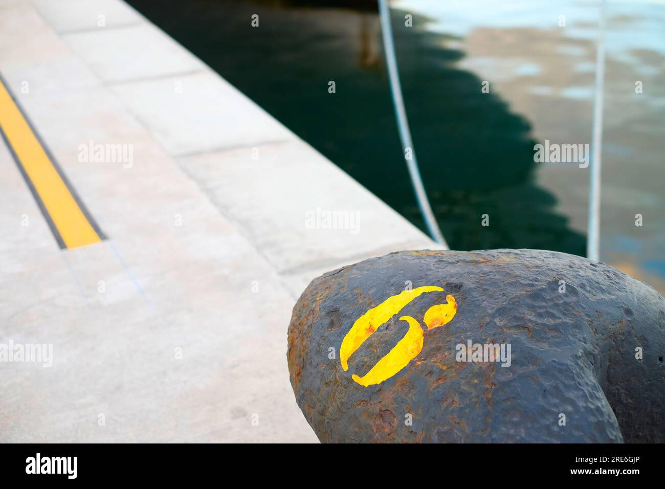 Numéro 6 en pochoir jaune sur une borne noire, et vue abstraite d'un amarrage dans un bassin portuaire commercial. Banque D'Images