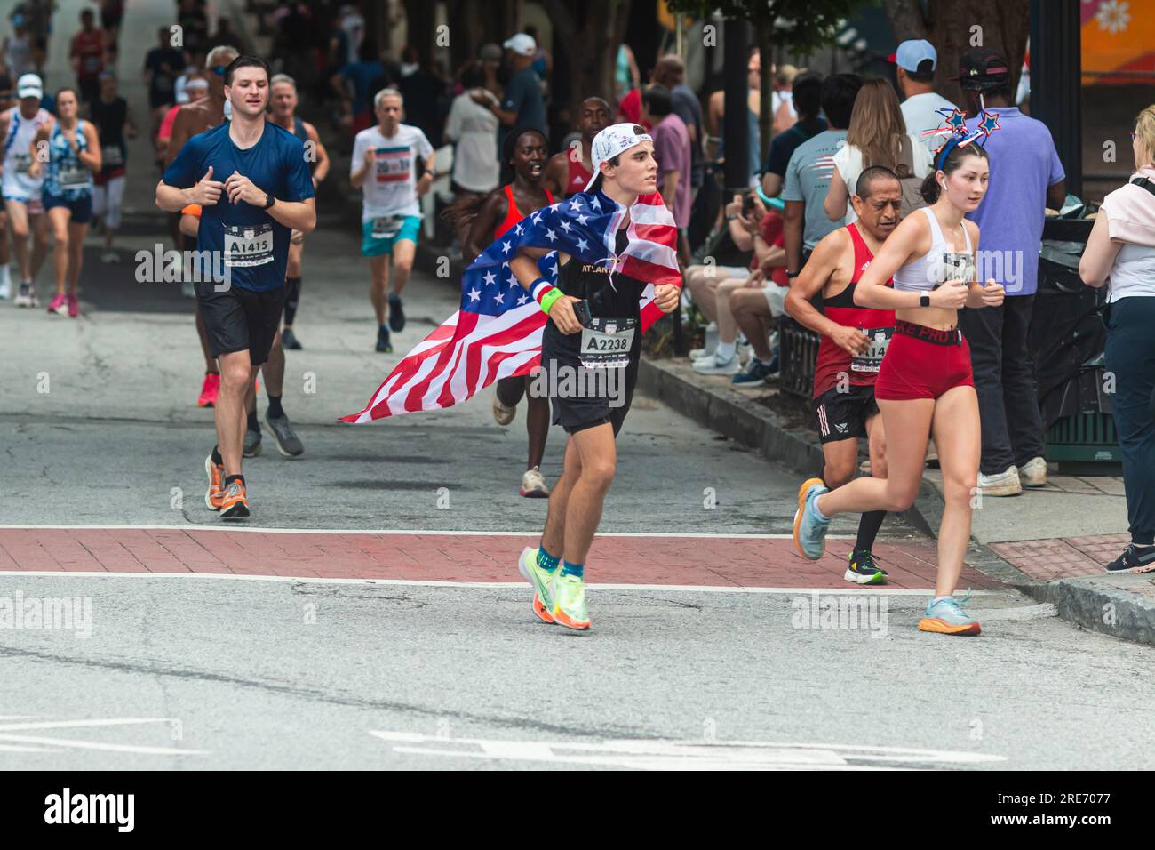Atlanta, GA / États-Unis – 4 juillet 2023 : un jeune homme porte un drapeau américain comme cape lors de la course Peachtree Road Race le 4 juillet 2023 à Atlanta, GA. Banque D'Images