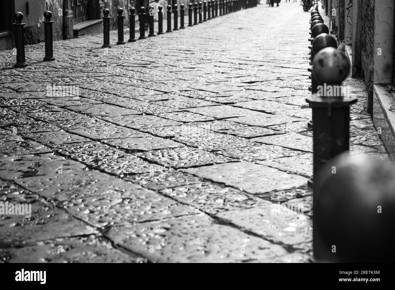 Nous rue pavée bordée de poteaux gris après une tempête de pluie à Naples, en Italie. Banque D'Images