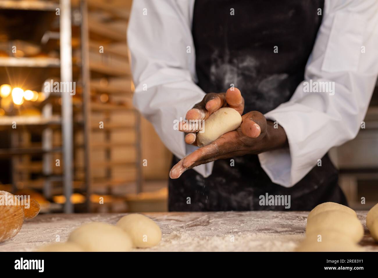 Boulanger mâle afro-américain dans la cuisine de boulangerie formant la pâte pour les rouleaux Banque D'Images